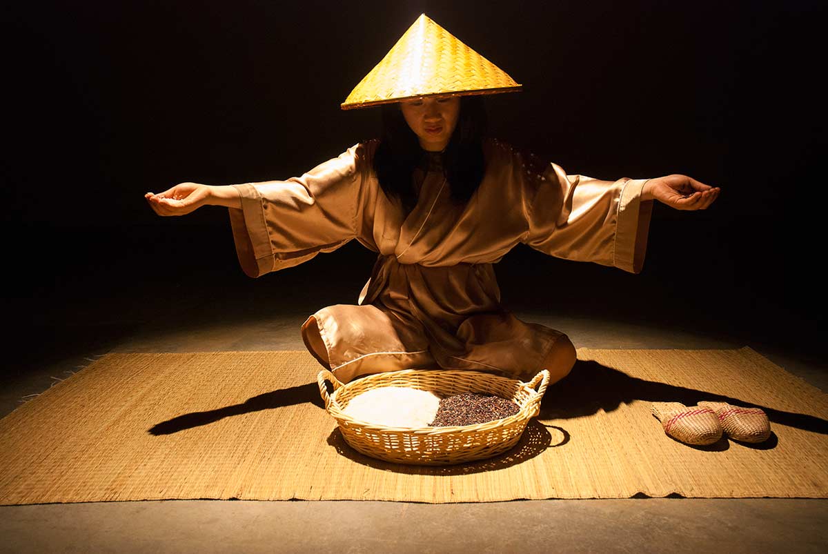 Chun Hua Catherine Dong sits in front of a sieve that is filled with black and white rice, she grabs the rice and starts to meditate her situation
