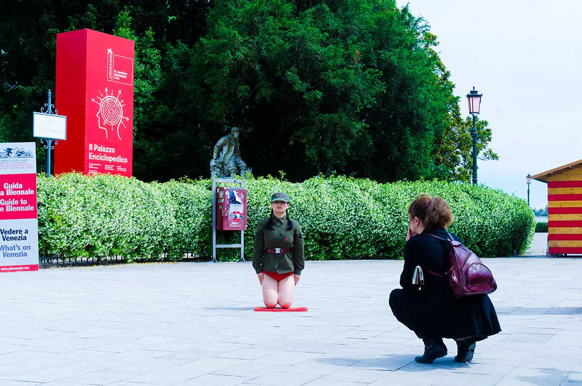 Chun Hua Catherine Dong wear a military suit and red underwear, kneeling on a washboard and keeping straight and still as long as she can in Venice Biennale in 2013