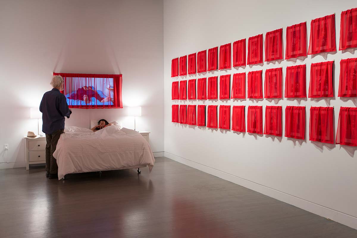 an audience came to Chun Hua Catherine Dong's bed and chatted with her when she stayed on her bed for 60 hours as part of her Husbands and I exhibition at Leonard & Bina Ellen Art Gallery in 2012