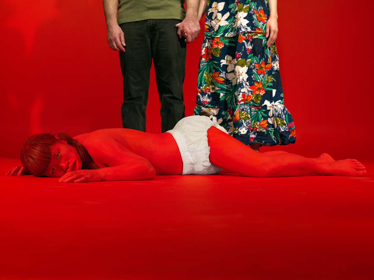 Chun Hua Catherine Dong painted her body red and wore diaper, living with strangers hired from Craigslist in a red room as their child. The red baby is lying on the floor like a hopeless baby