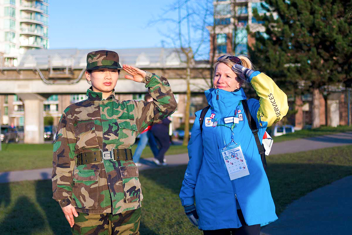 Chun Hua Catherine Dong wears military suit and salutes with her left hand, a wrong hand, to Olympic symbols. she invites people to salute with her
