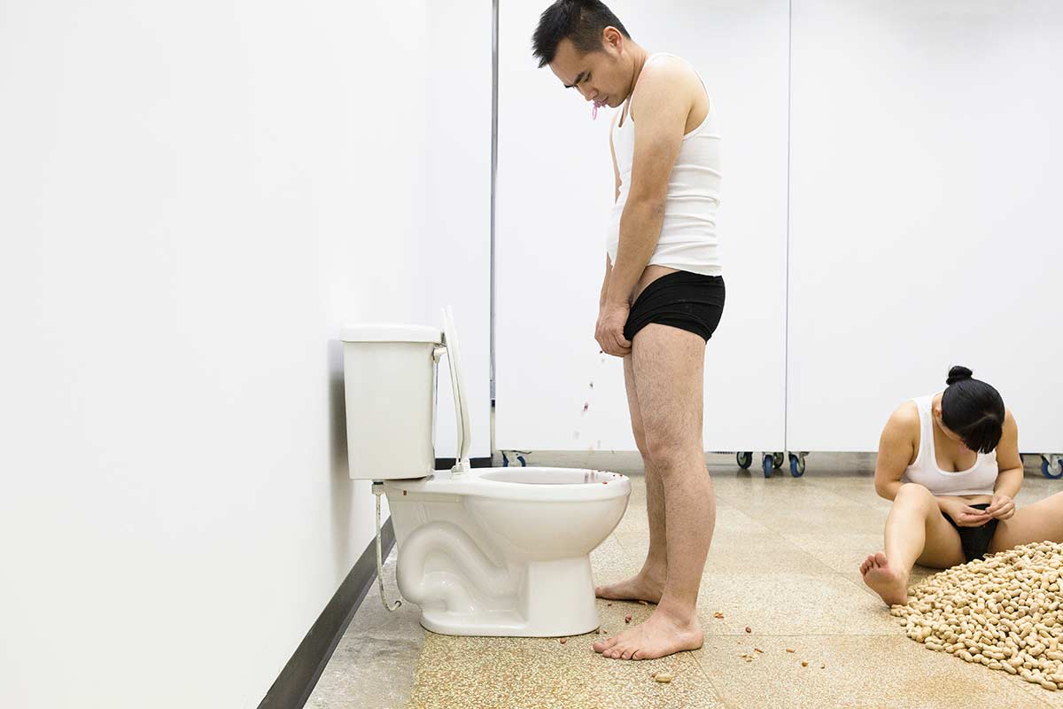 Chun Hua Catherine Dong is shucking peanuts while her performance partner is dumping peanut seeds into a toilet