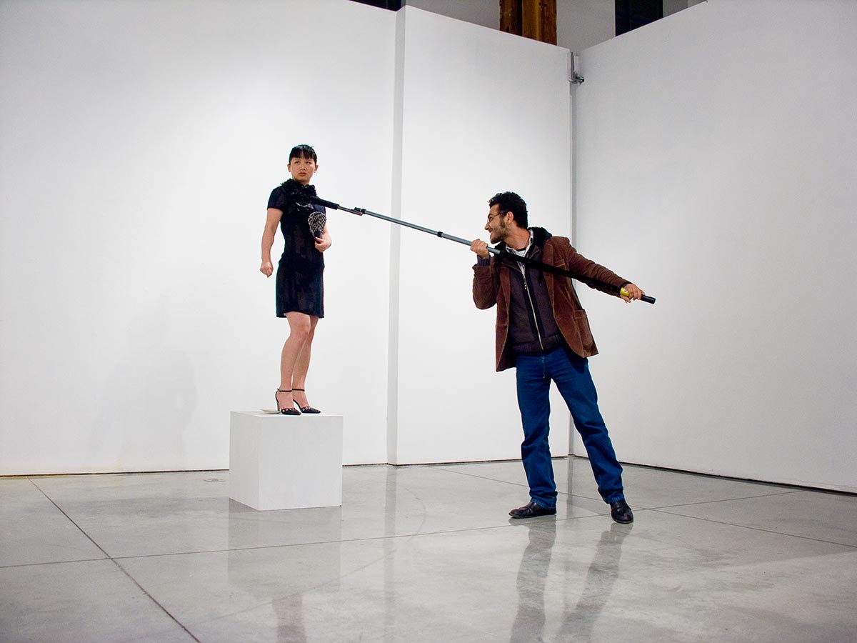 Chun Hua Catherine Dong stands on a plinth and holds her fist,  when the viewers use a boom microphone to inspect my body, sharp sounds will occur