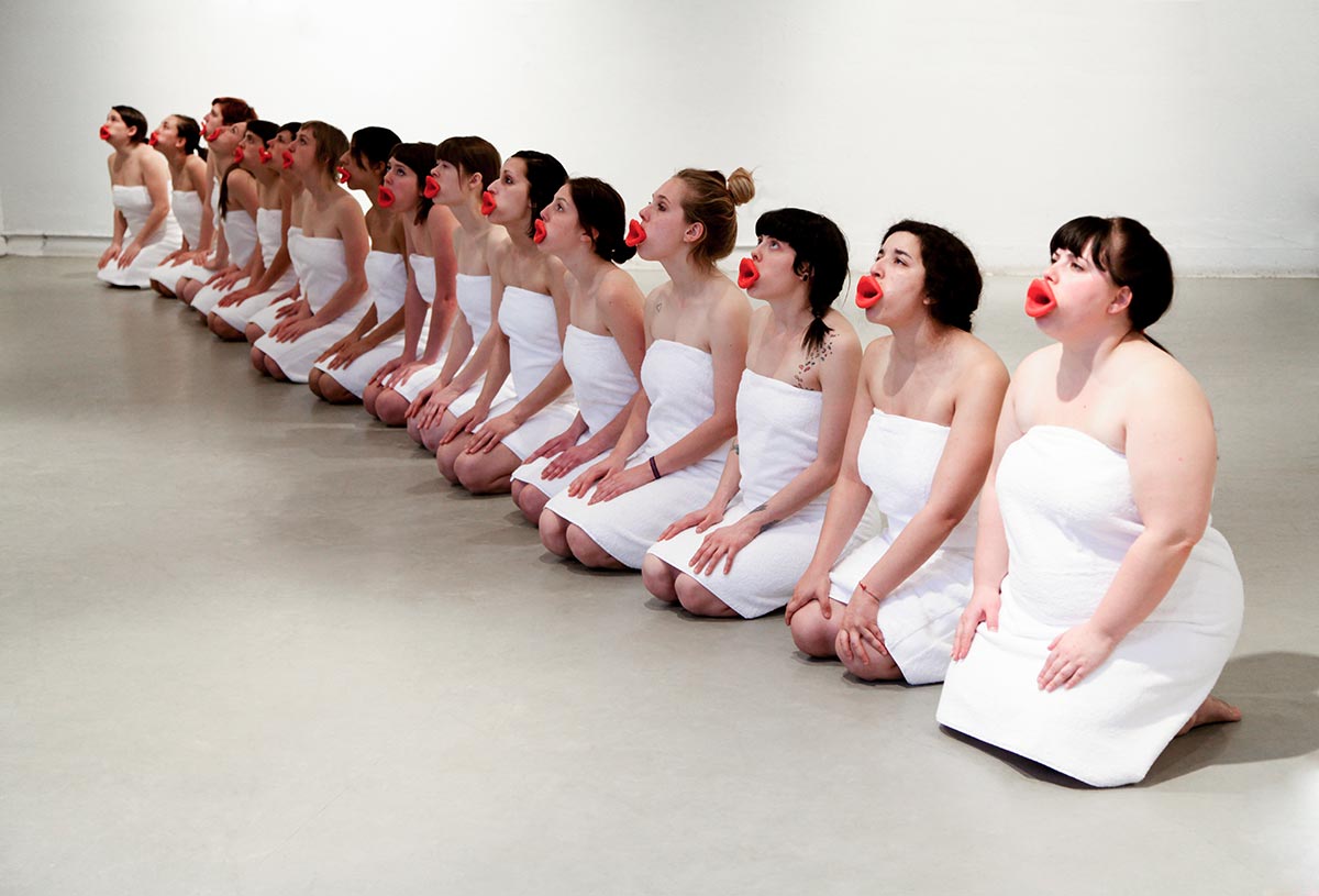 Chun Hua Catherine Dong's performance: Sixteen girls wear red mouthpieces and white bath towels, standing in a row, repeating  three still gestures: standing, kneeing, and lying on the floor.