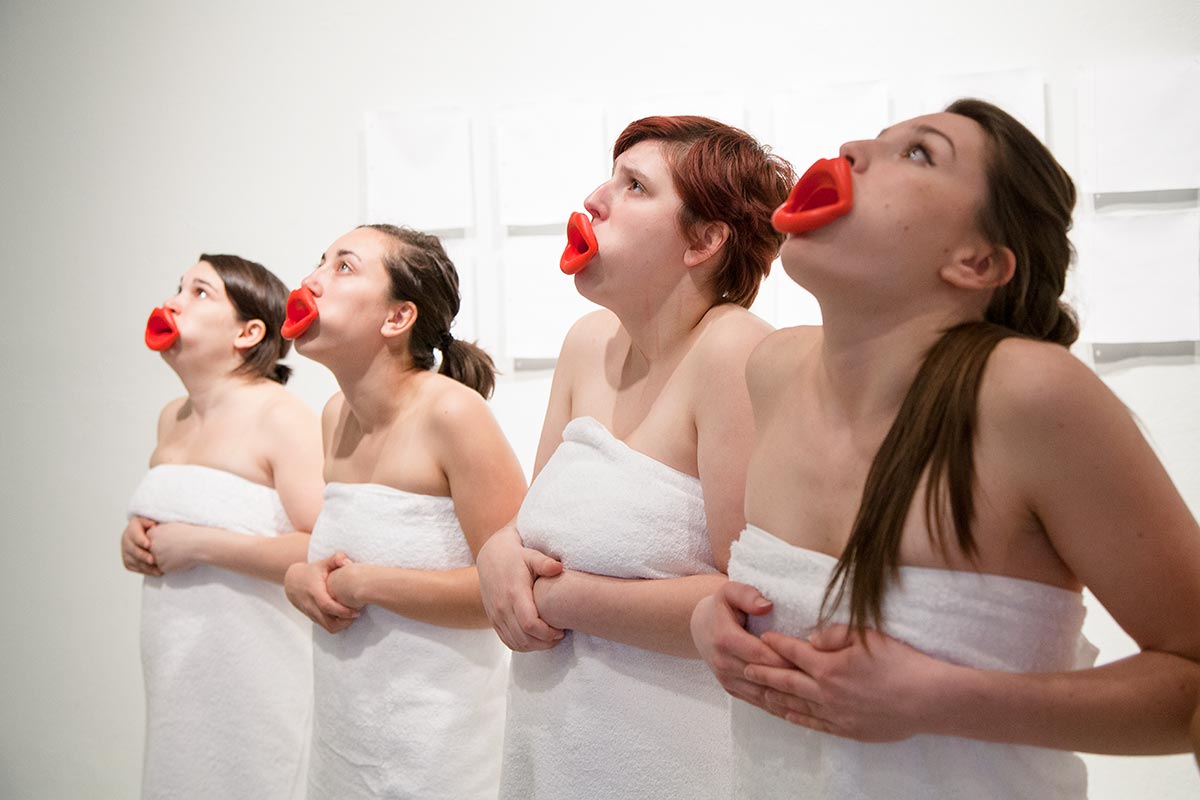 Chun Hua Catherine Dong's performance: Sixteen girls wear red mouthpieces and white bath towels, standing in a row, repeating  three still gestures: standing, kneeing, and lying on the floor.