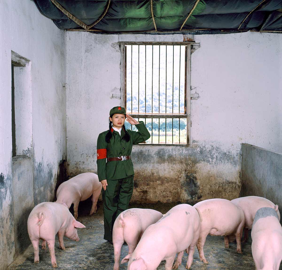 Chun Hua Catherine Dong performs the Red Guard in the Chinese Cultural Revolution. she salutes with her left hand in a pig house