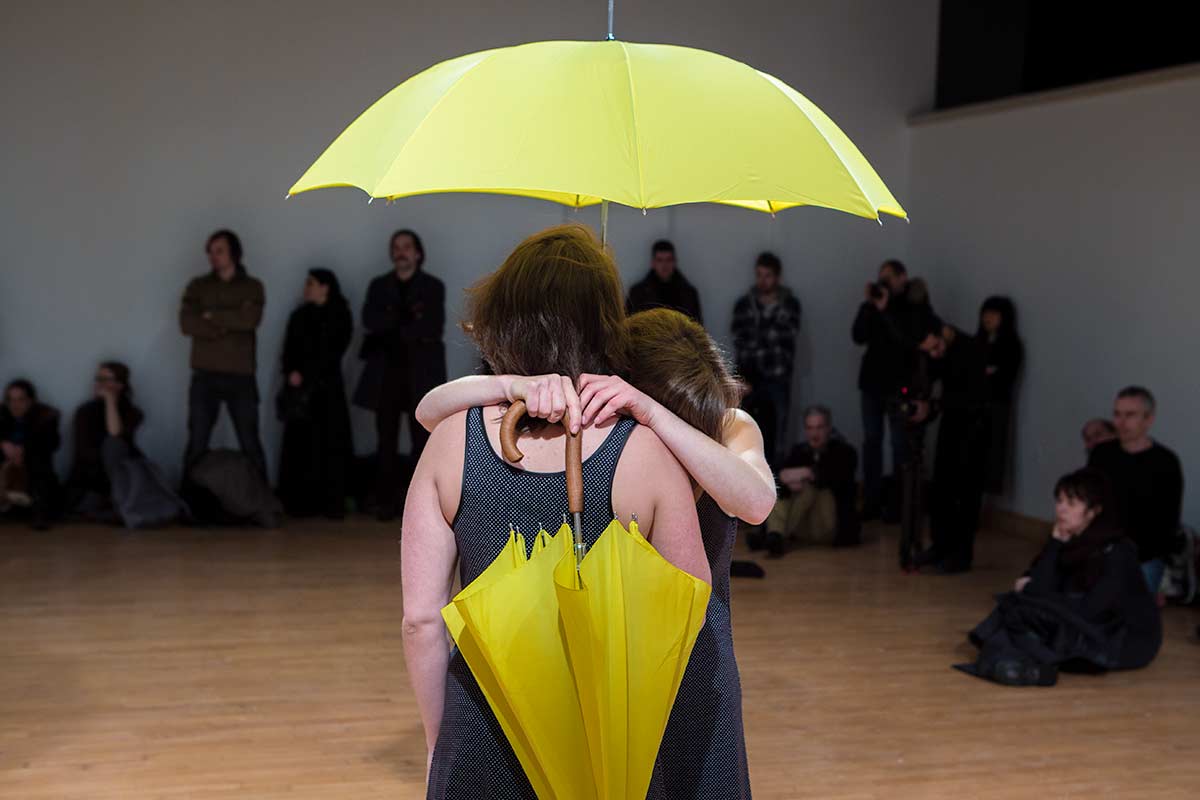 Chun Hua Catherine Dong's Yellow Umbrella performance in Montreal: 2 females hold yellow umbrellas and hug each other 