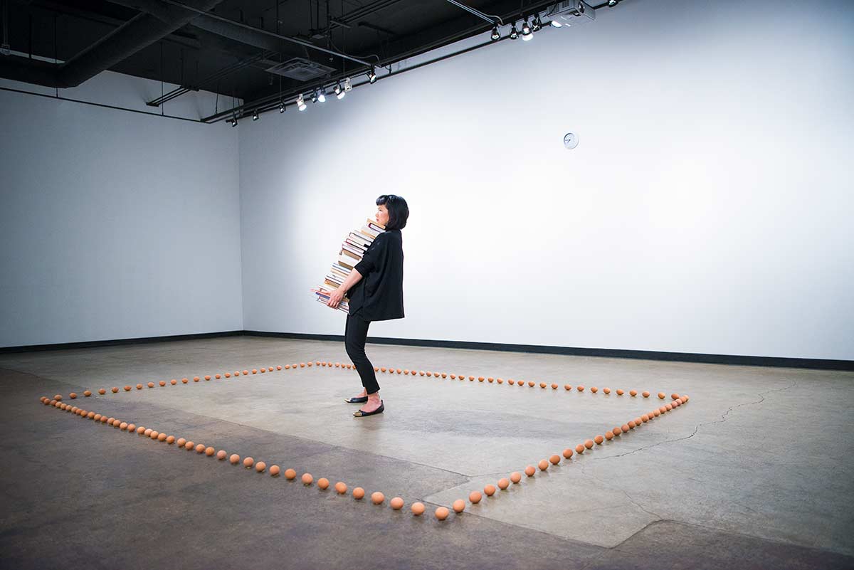 Chun Hua Catherine Dong stands in the centre of a rectangle that is made by eggs, holding a stack of books
