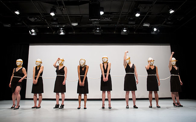 Chun Hua Catherine Dong ties eight dancers together with a rope, the dancers wear masks, standing in a row and repeating some symbolic gestures in relations to shame and vulnerability.