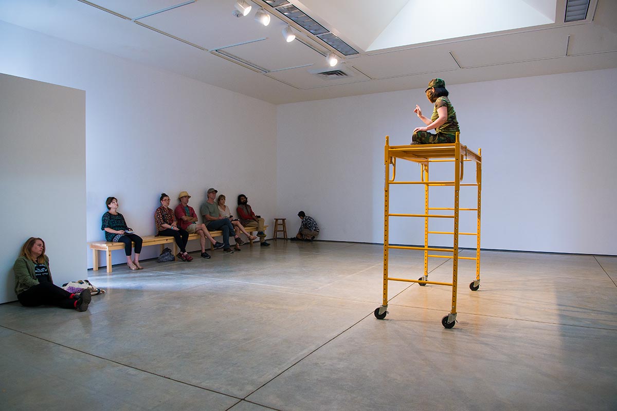 Chun Hua Catherine Dong wears a hairy strange mask and points at her audiences