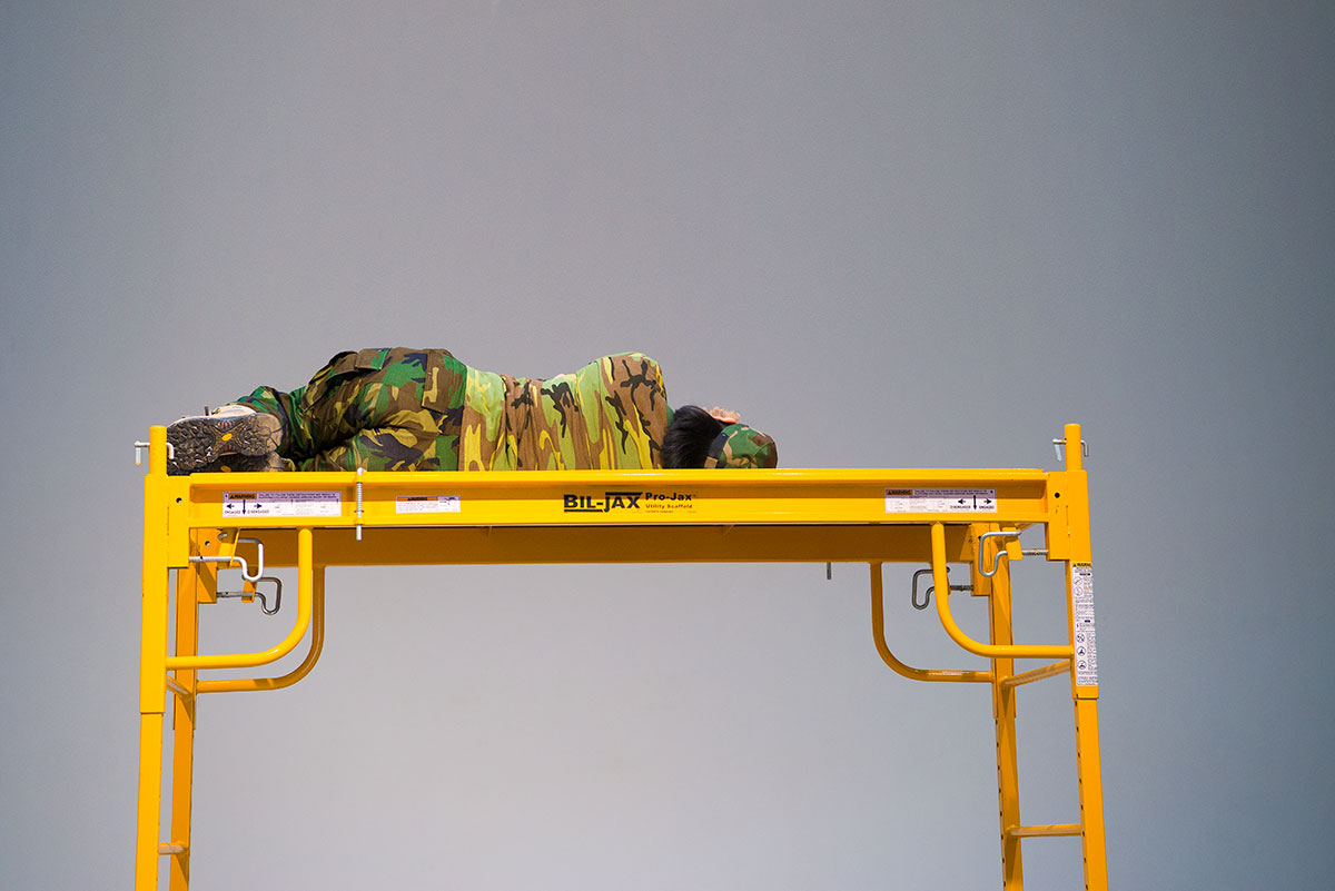Chun Hua Catherine Dong wears military suit, lying on a scaffold