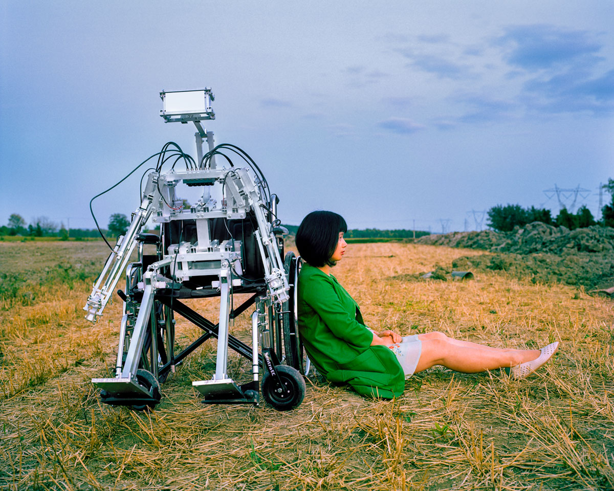 Chun Hua Catherine Dong sits beside  a robot in a evening 