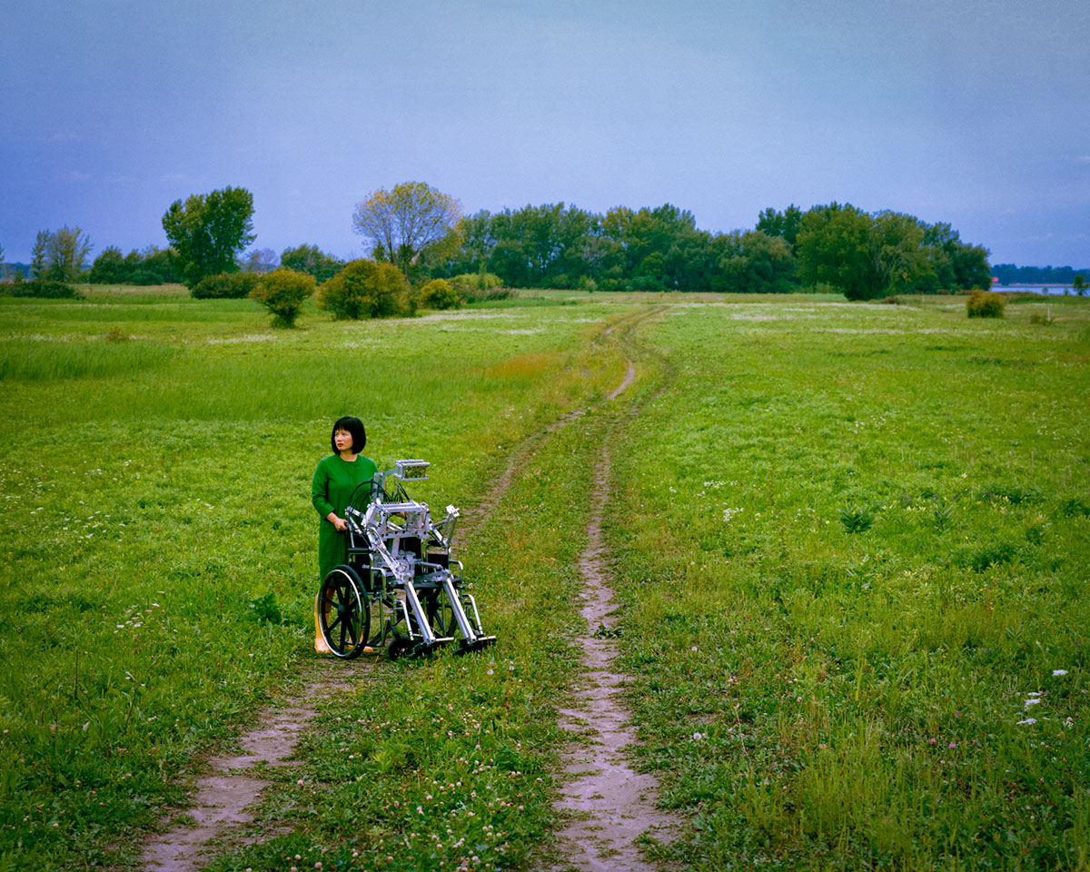 Chun Hua Catherine Dong pushes a robot in a wheelchair in a countryside