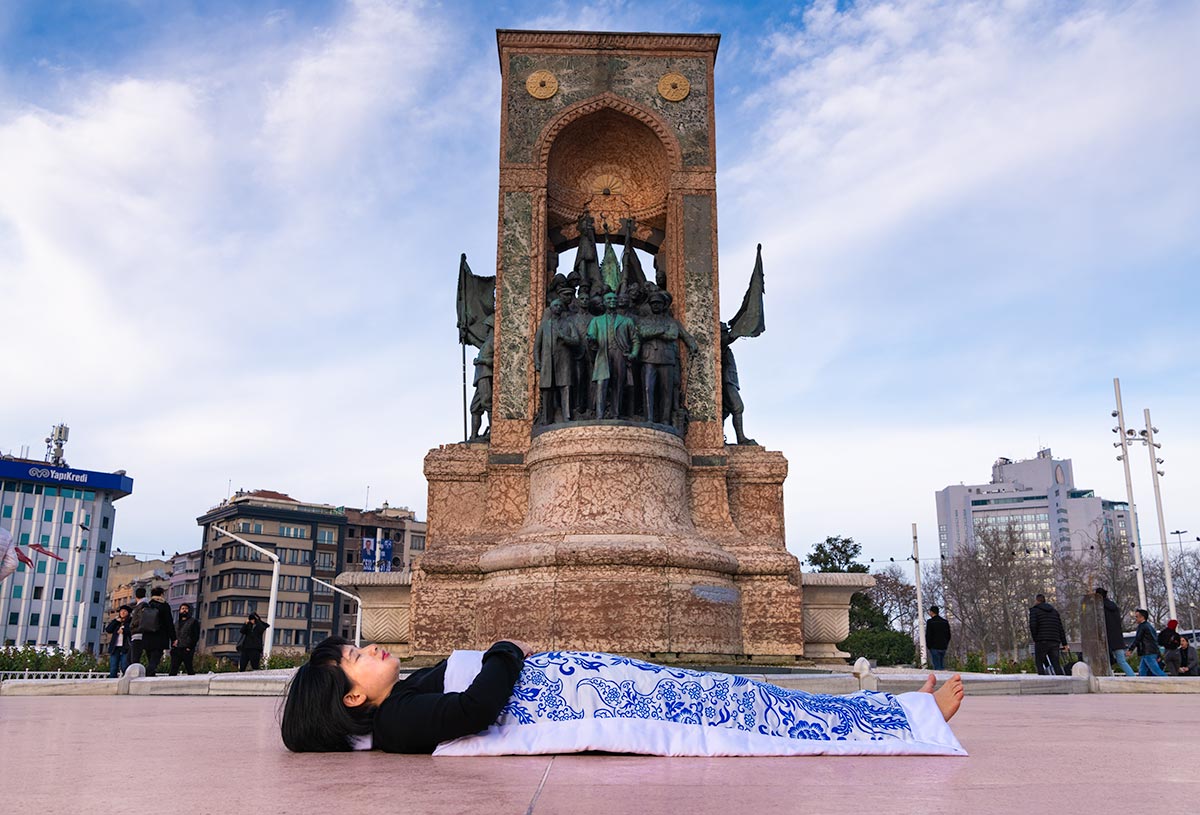 Chun Hua Catherine Dong covers herself with a duvet and performs death ritual  at Taksim Square in Istanbul