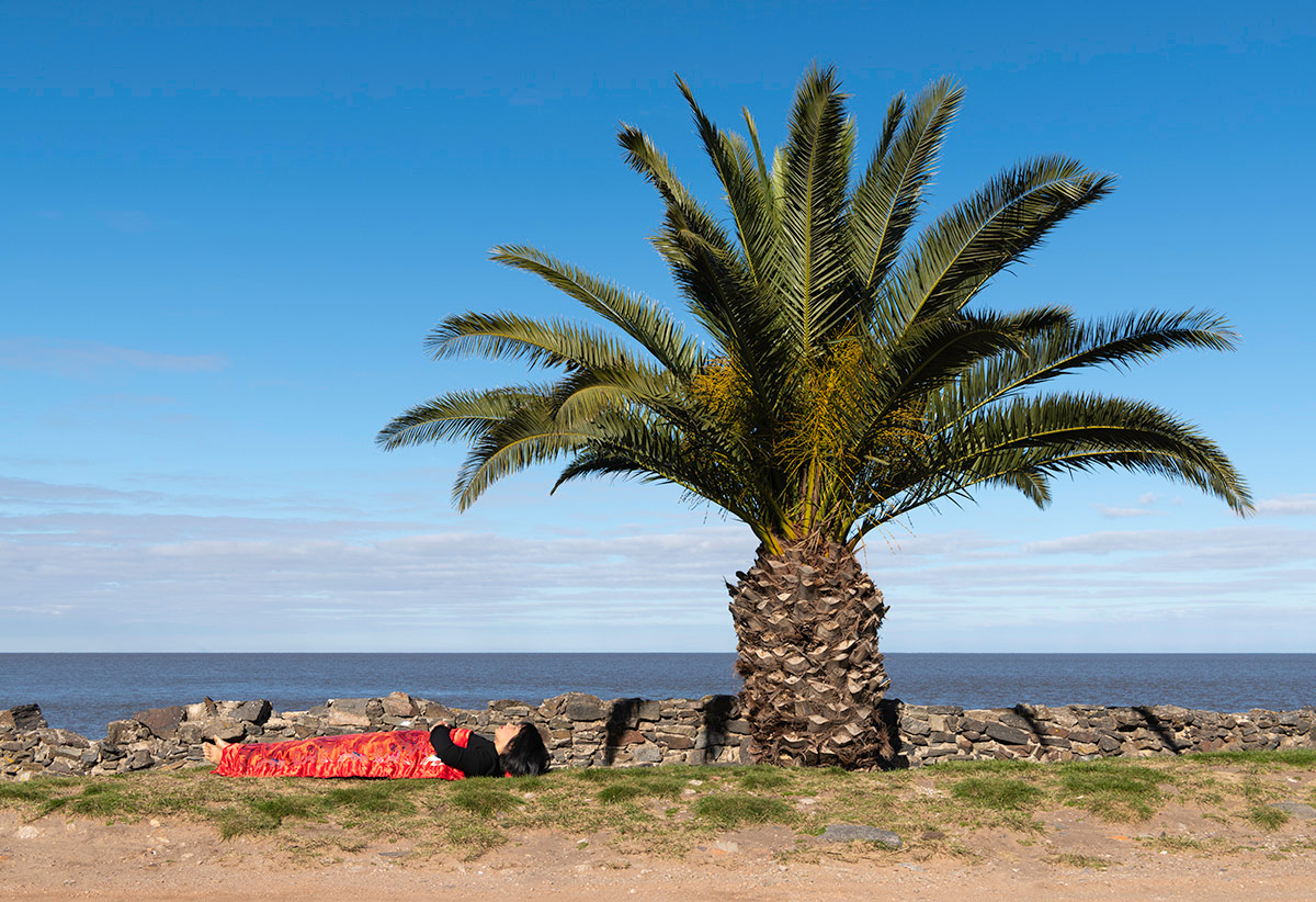 Chun Hua Catherine Dong sleeps under a big palm tree and sea in Colonia del Sacramento, Uruguay