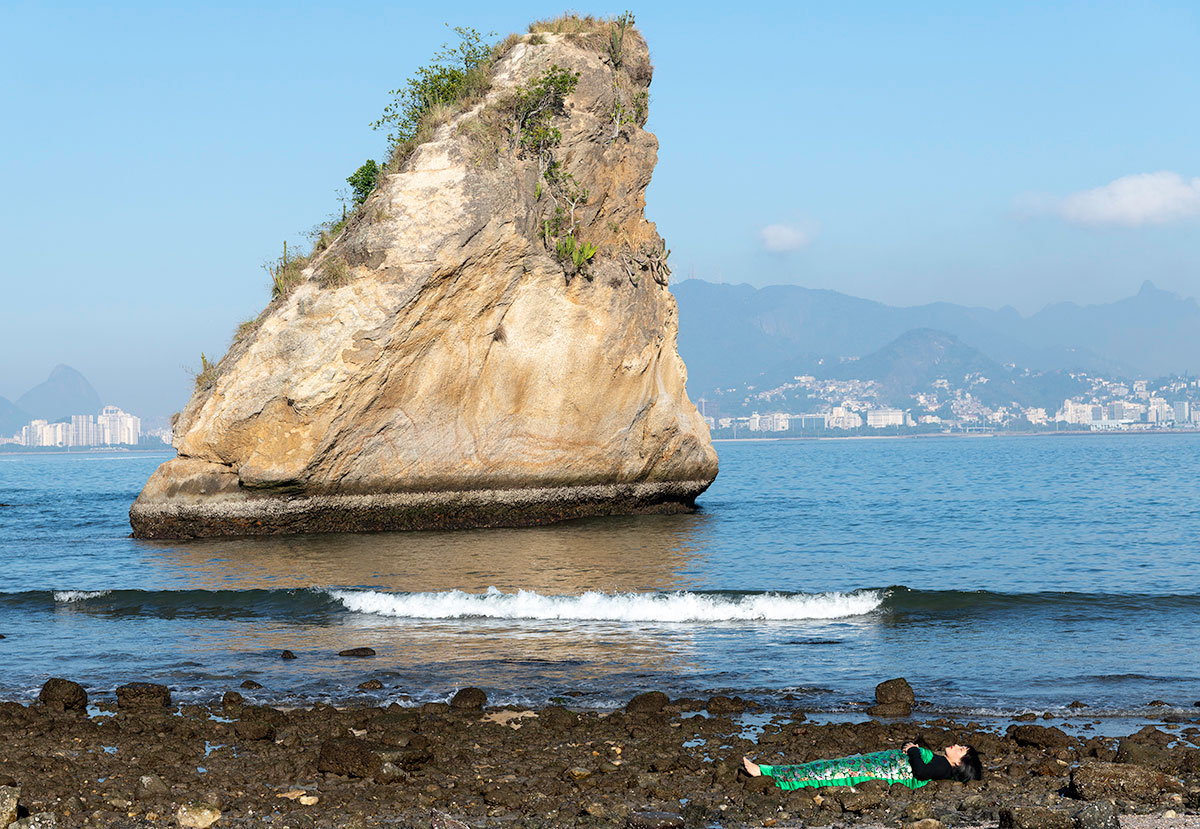 Chun Hua Catherine Dong sleeps beside the sea in front of a big rock in Rio de Janeiro