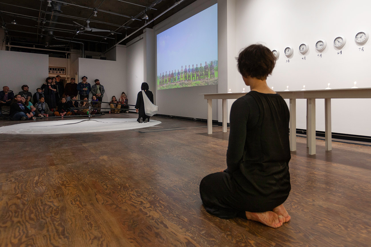 Chun Hua Catherine Dong kneels on salt and walk with the clock backwards at Neutral Ground Gallery