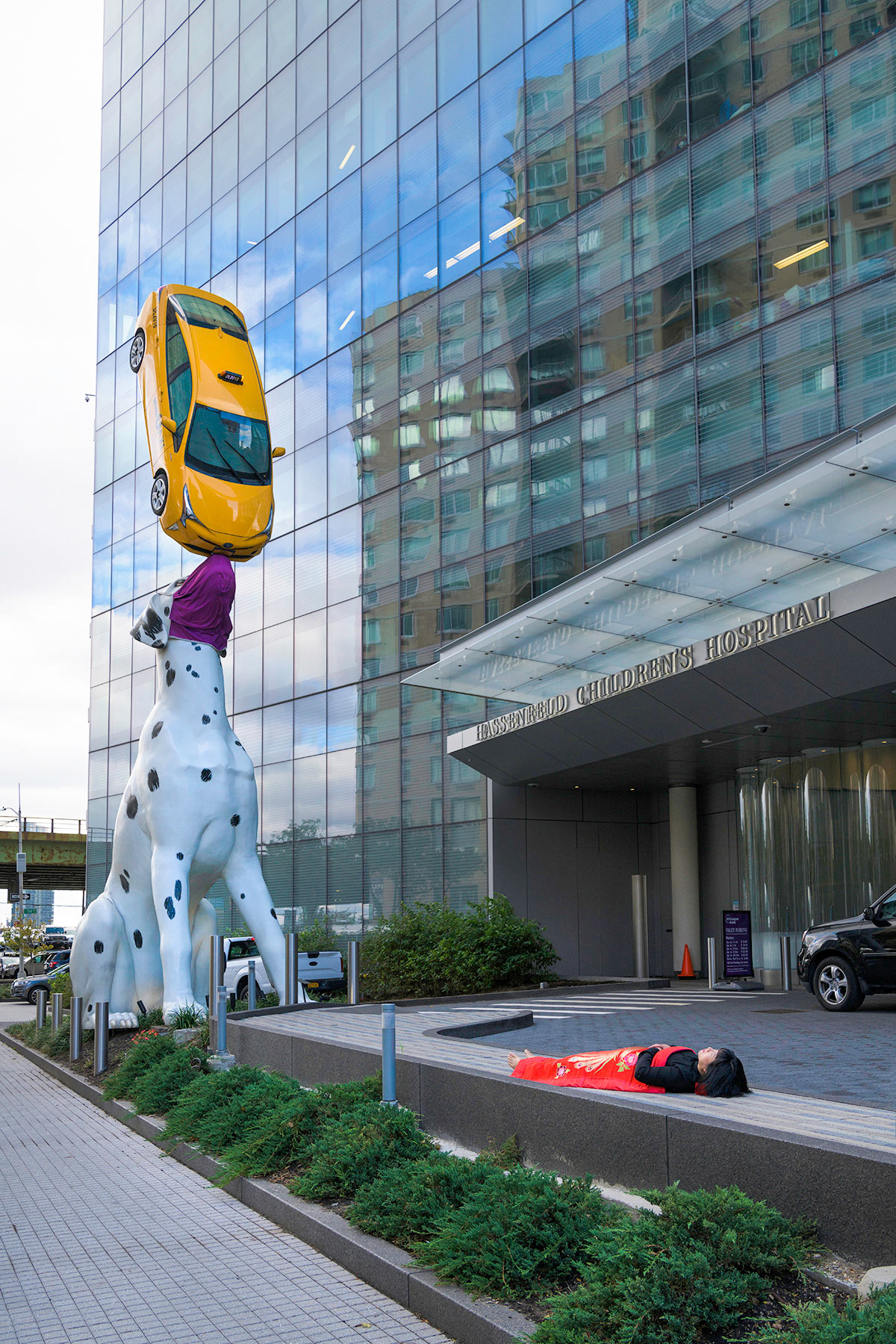 Chun Hua Catherine Dong sleeps in front of a dog and taxi sculpture n New York City