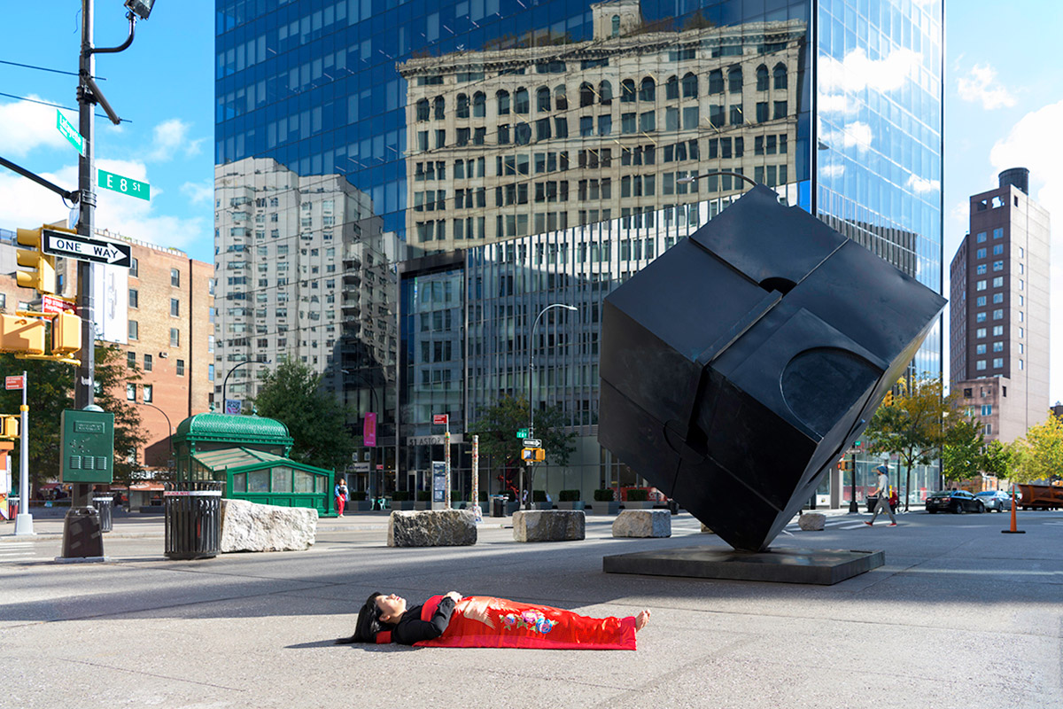 Chun Hua Catherine Dong sleeps in front of a black cube sculpture in New York City