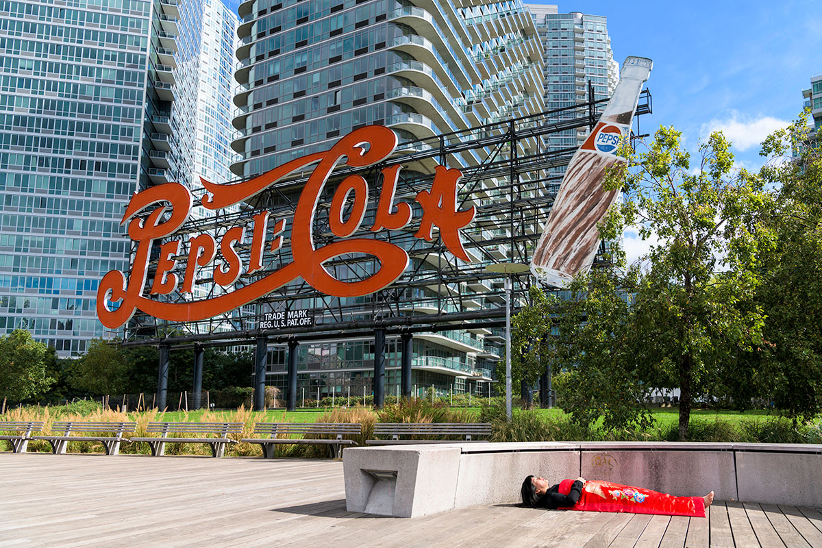 Chun Hua Catherine Dong sleeps in front of Pepsi Coke sign in New York City