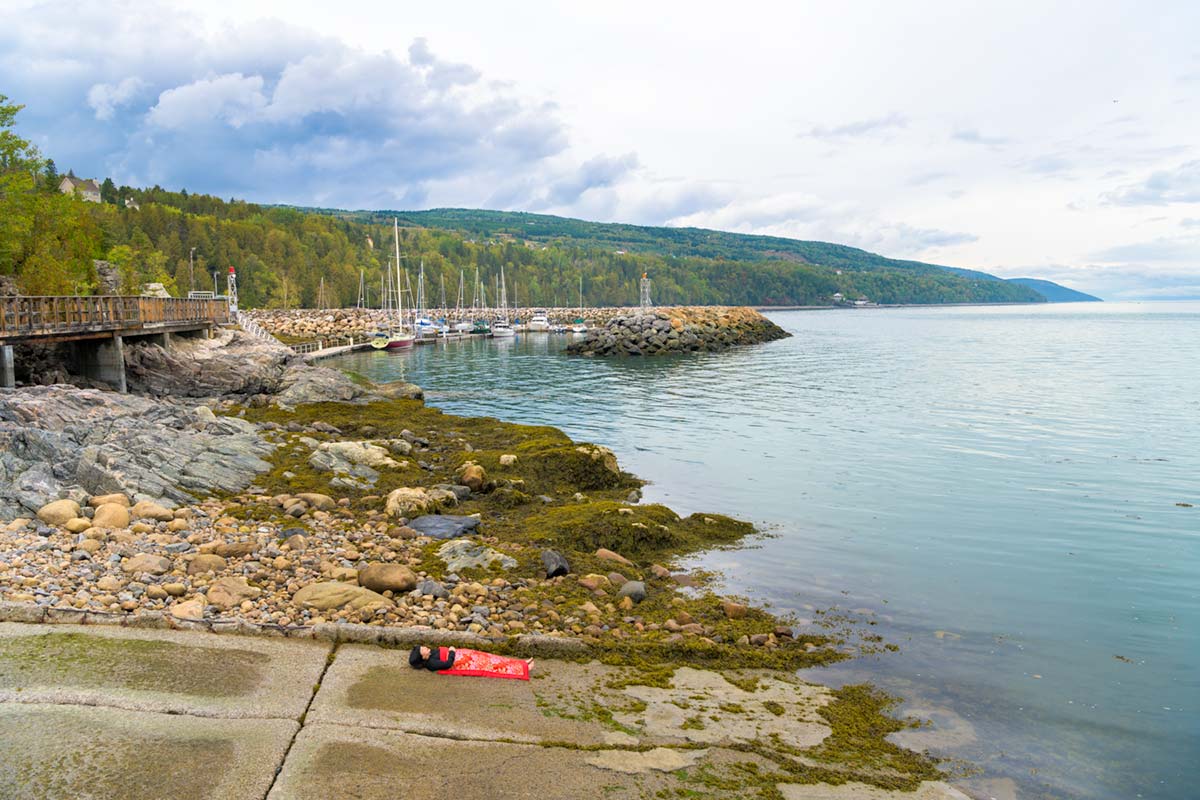 a girl is covered by a red blanket and lies beside Saint Lawrence River