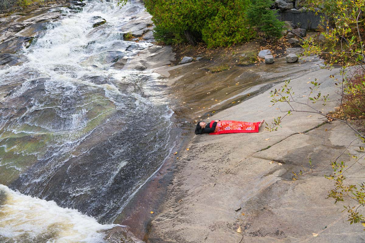 a girl is covered by a red blanket and lies beside Saint Lawrence River