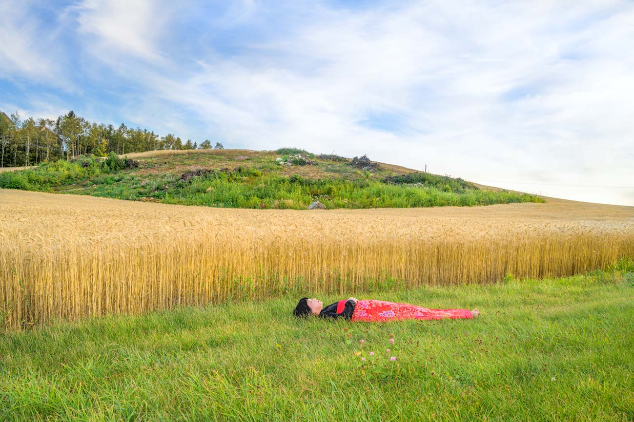 a girl is covered by a red blanket and lies on a rice field