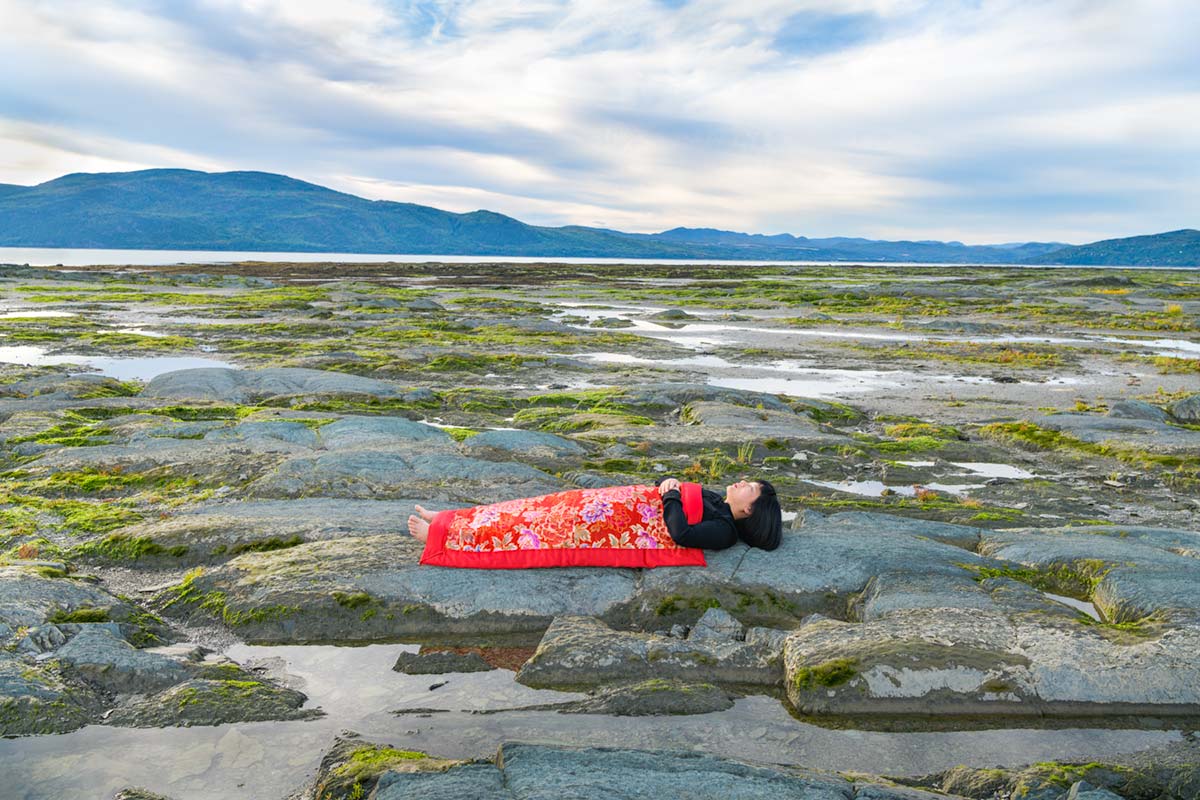 a girl is covered by a red blanket and lies beside Saint Lawrence River