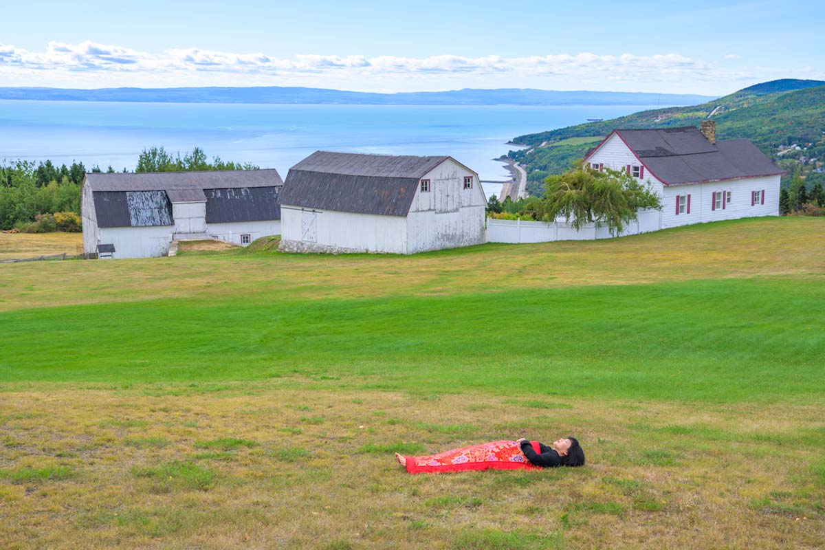 a girl is covered by a red blanket and lies beside Saint Lawrence River in front of houses