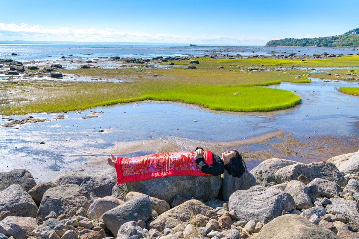 a girl is covered by a red blanket and lies beside Saint Lawrence River