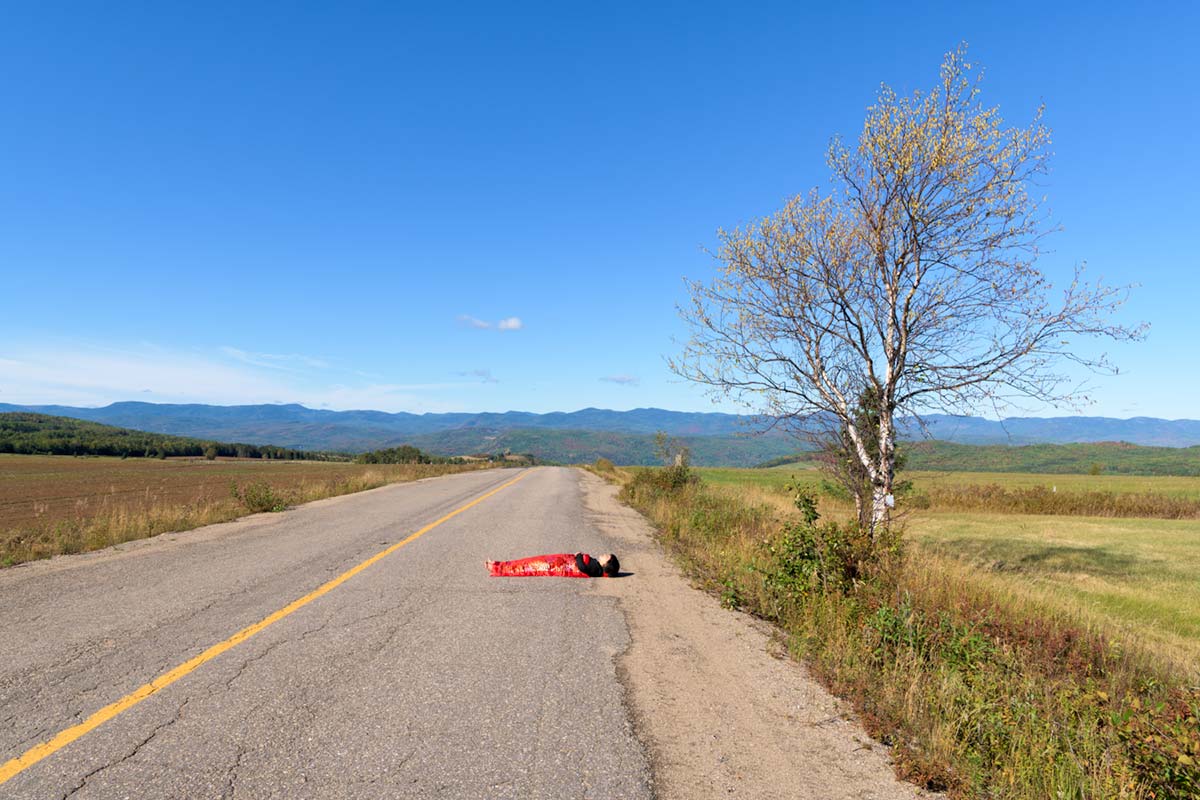 a girl is covered by a red blanket and lies on a road with a tree