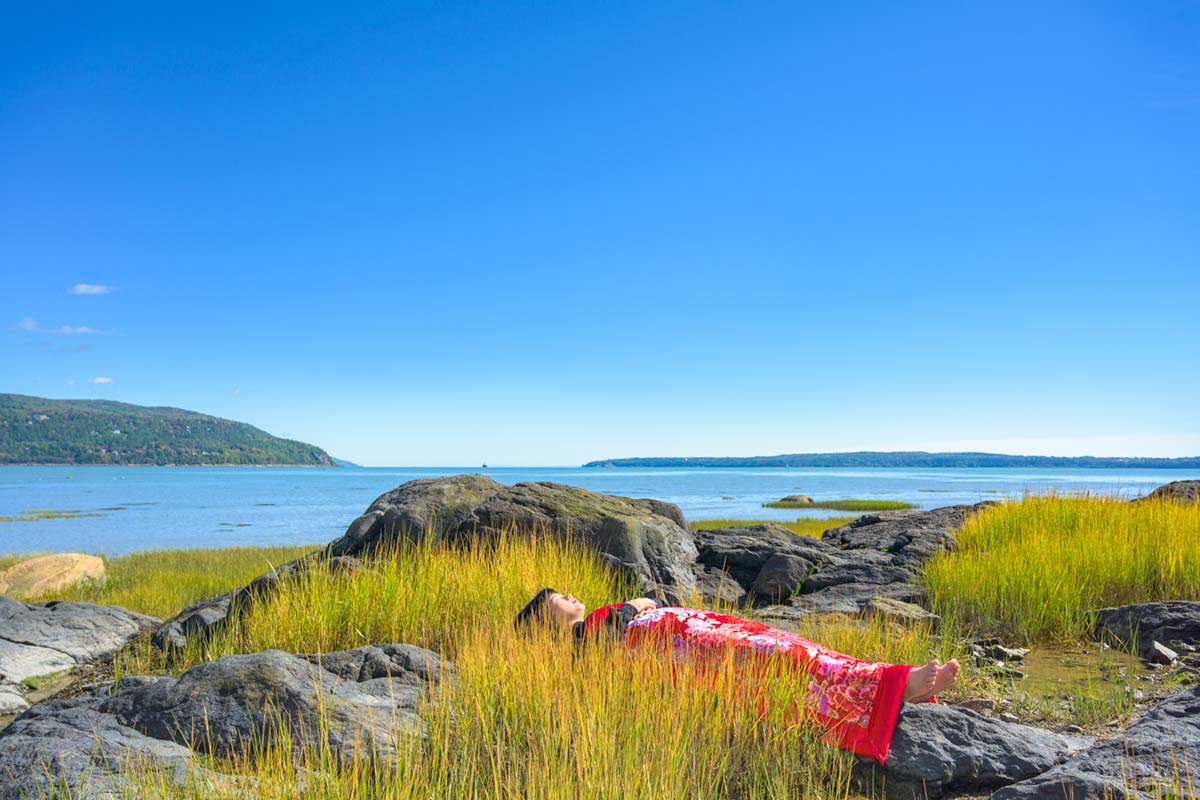 a girl is covered by a red blanket and lies beside Saint Lawrence River