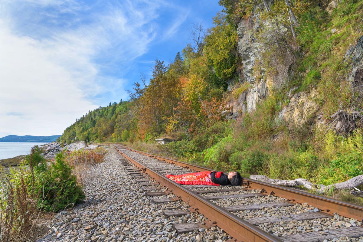 a girl is covered by a red blanket and lies beside Saint Lawrence River on a railway