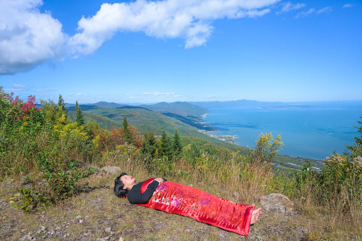 a girl is covered by a red blanket and lies beside Saint Lawrence River