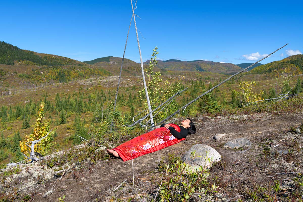 a girl is covered by a red blanket and lies in a mountain