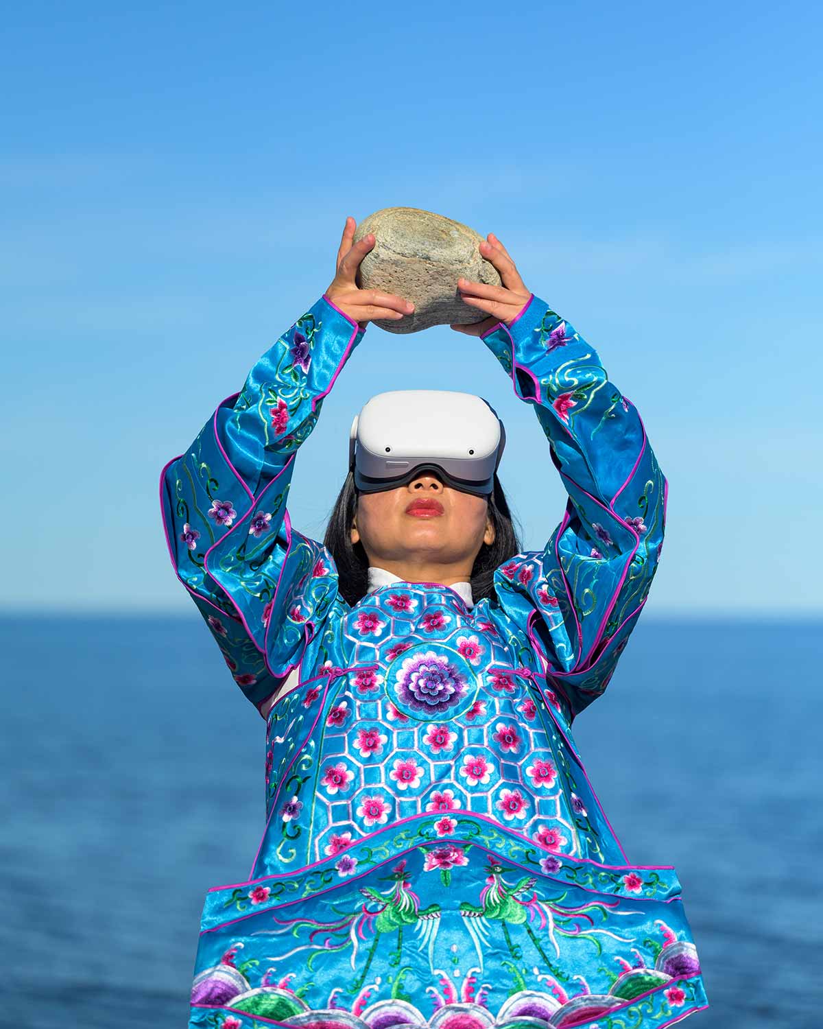 Chun Hua Catherine Dong wears Oculus VR headset and a blue Chinese opera costume with a stone on her hands beside The St. Lawrence River.