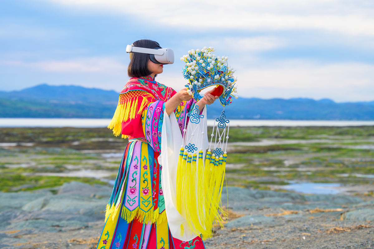 Chun Hua Catherine Dong wears Oculus VR headset and a red Chinese opera costume with a phoenix crown on her hands beside the St. Lawrence River.