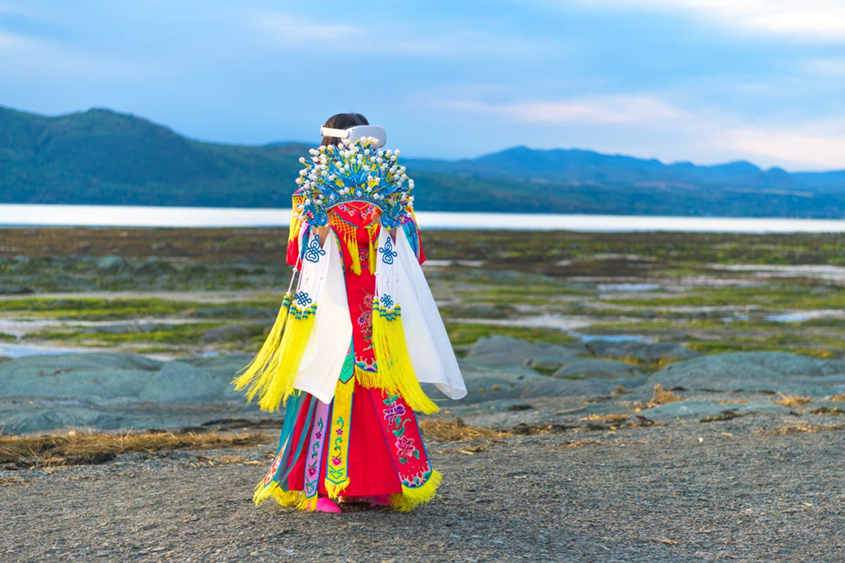 Chun Hua Catherine Dong wears Oculus VR headset and a red Chinese opera costume with a phoenix crown on her hands beside the St. Lawrence River.