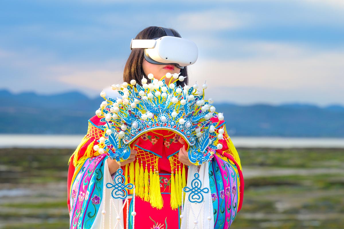 Chun Hua Catherine Dong wears Oculus VR headset and a red Chinese opera costume with a phoenix crown on her hands beside the St. Lawrence River.