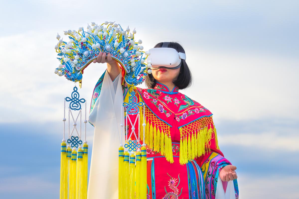 Chun Hua Catherine Dong wears Oculus VR headset and a red Chinese opera costume with a phoenix crown on her hand beside the St. Lawrence River.