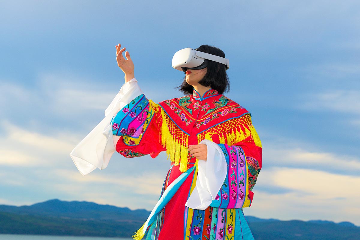 Chun Hua Catherine Dong wears Oculus VR headset and a red Chinese opera costume beside The St. Lawrence River.