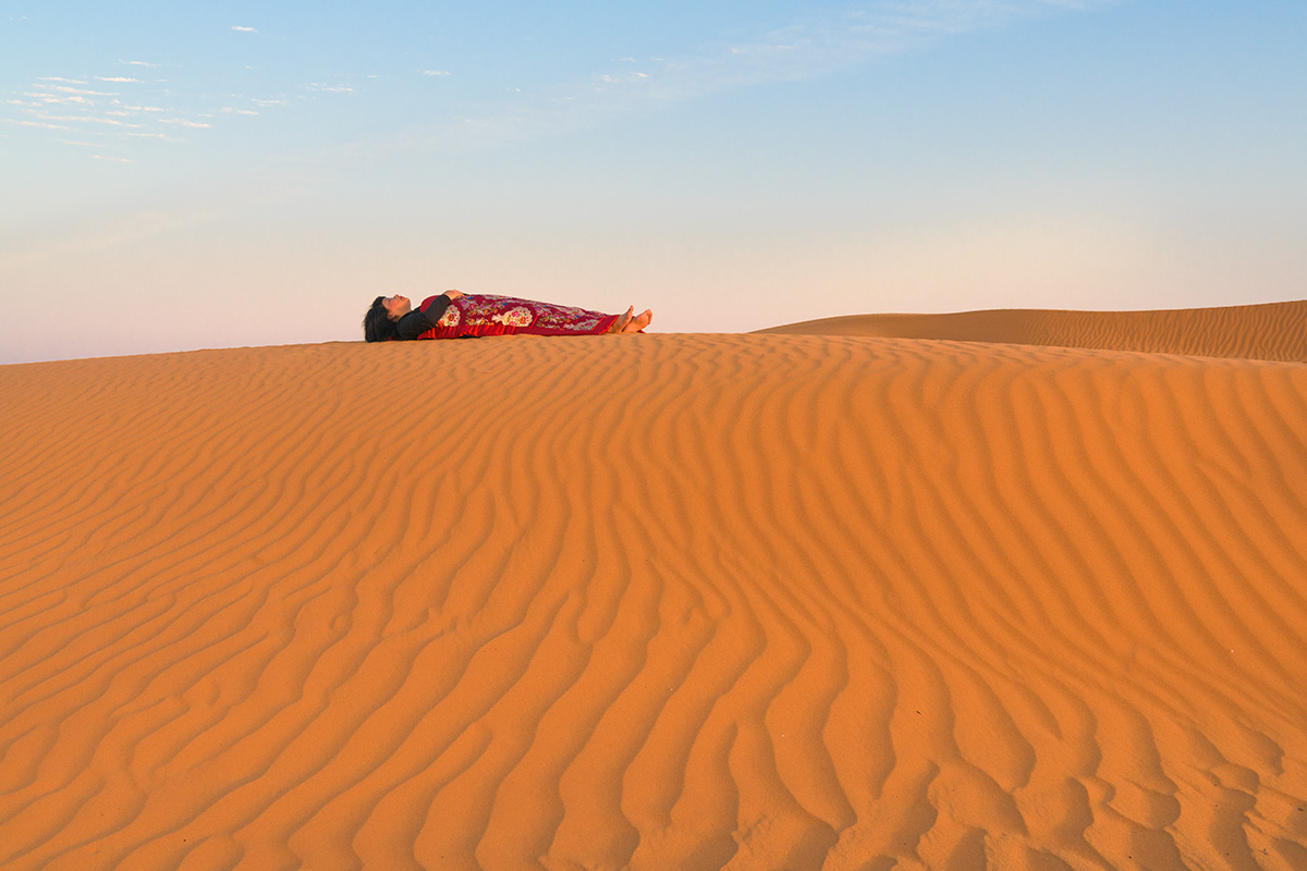 Chun Hua Catherine Dong’s body is covered by a Chinese red blanket, Dong lies on top of red sand on Red Sand Dunes in Riyadh, Saudi Arabia.