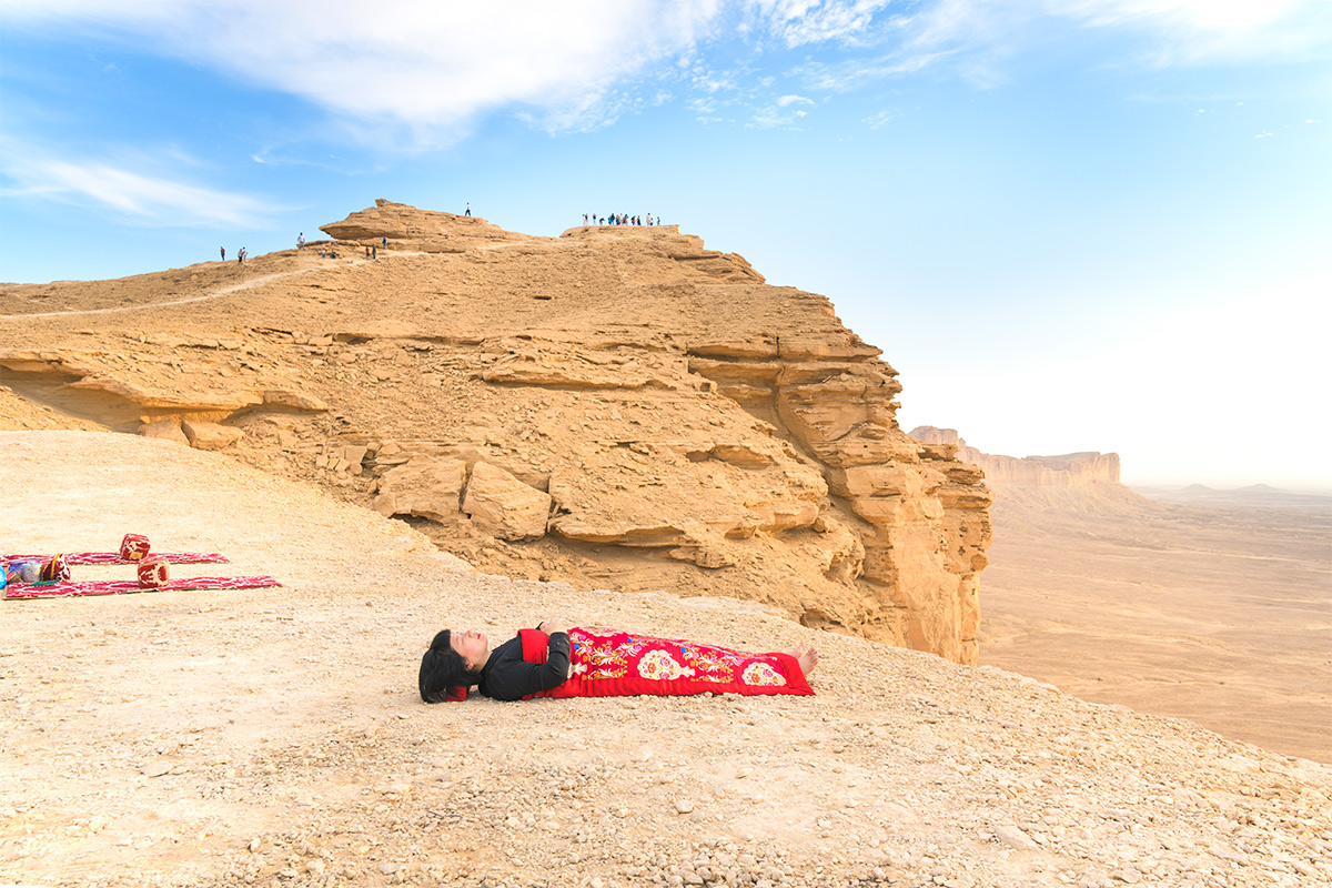 Chun Hua Catherine Dong sleeps at edge of the world, Riyadh, Saudi Arabia, her body is covered with a Chinese red blanket.