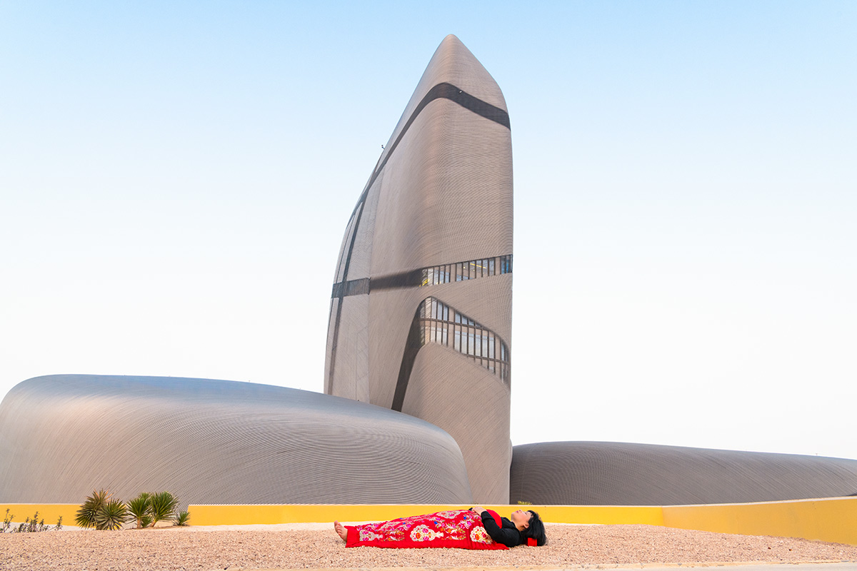 Chun Hua Catherine Dong sleeps in front of strange architecture, King Abdulaziz Center for World Culture – Ithra, Damman, Saudi Arabia, her body is covered with a Chinese red blanket