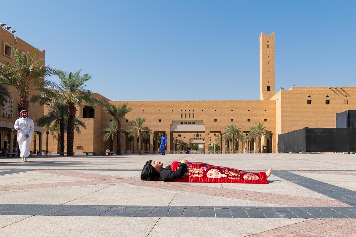 Chun Hua Catherine Dong sleeps in front of Imam turki bin aboullah grand mosque, Riyadh, Saudi Arabia, her body is covered with a Chinese red blanket.