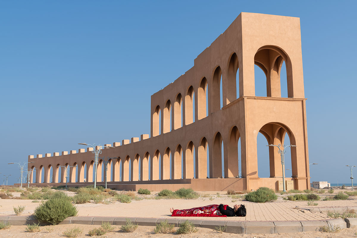 Chun Hua Catherine Dong sleeps in front of a strange architecture, Damman, Saudi Arabia, her body is covered with a Chinese red blanket