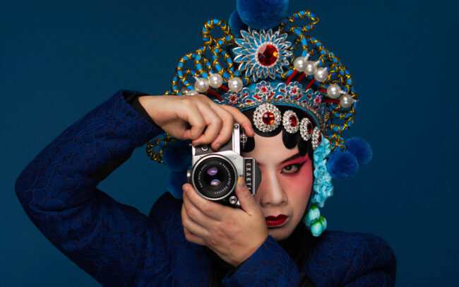 a woman wearing Beijing Opera headpiece while holding an old camera