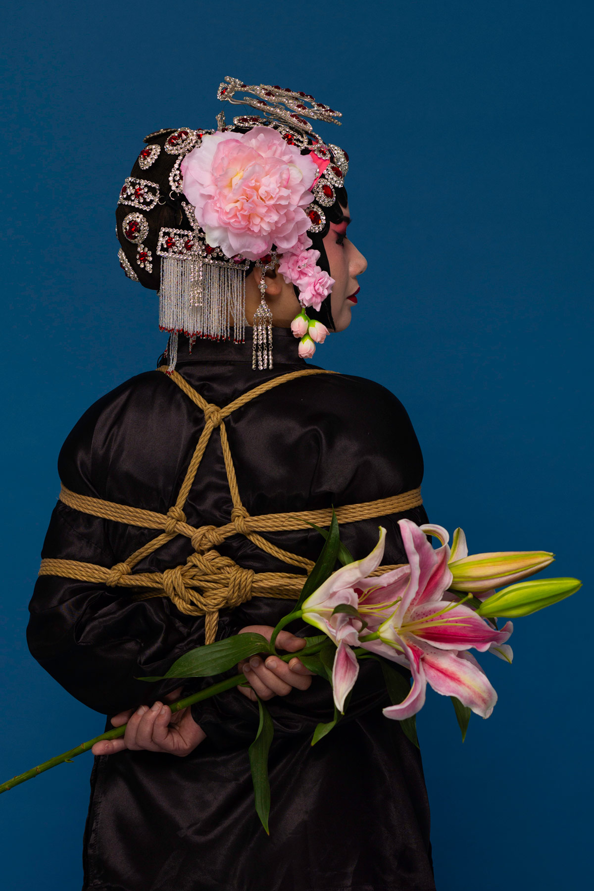 a girl wearing Beijing Opera costume with shaved head holding pink lily flower
